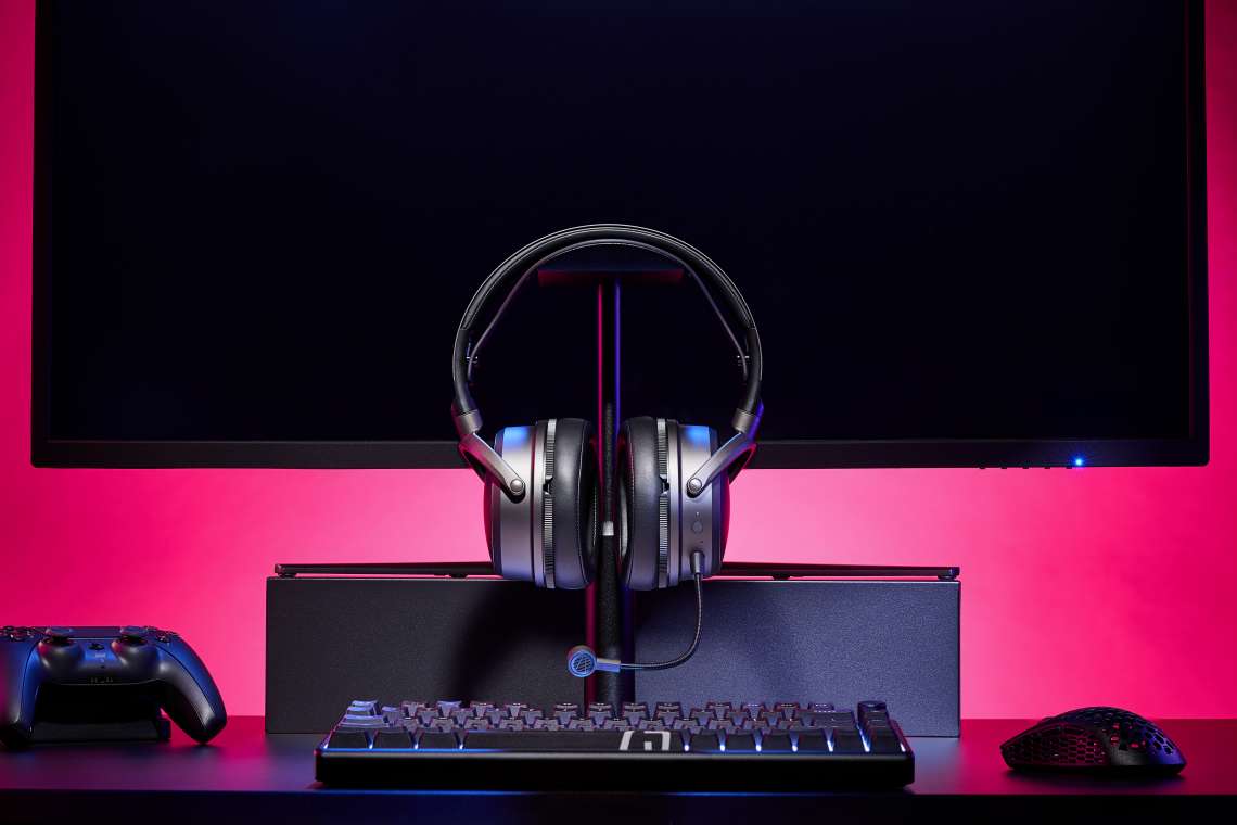 Słuchawki gamingowe Audeze Maxwell 2 na tle komputera i monitora, czerwone podświetlenie